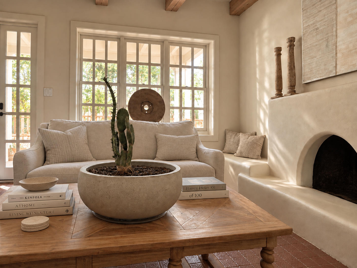 The Adobe living room with a sculptural fireplace, cactus planter, wood coffee table and window wall